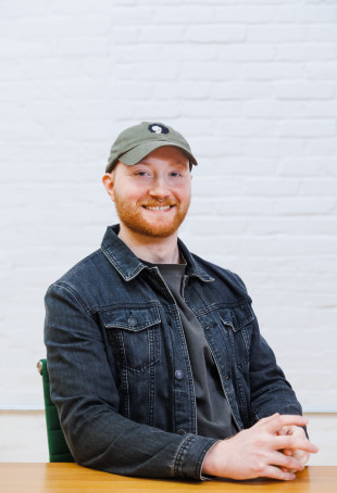 Sam smiling, wearing a green baseball hat and dark denim jacket.