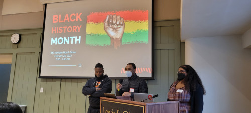 Three students from Black Student Union behind podium speaking for Black History Month Dinner.