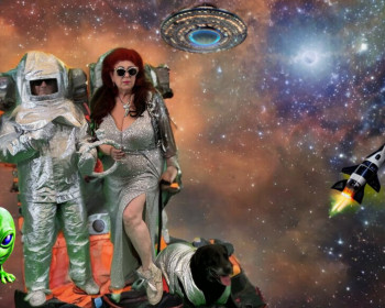 Beth Stephens and Annie Sprinkle in astronaut suits and an alien to the left, their dog to the right. 