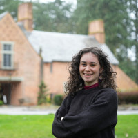 Lena posing in front of the Manor House, wearing a dark grey sweater.
