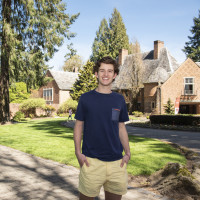 Bennett smiling outside by the Manor House on the undergraduate campus. He is wearing a navy tshirt and yellow shorts.