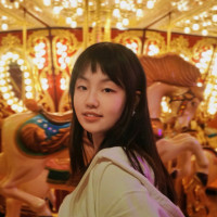 Polly smiling in front of a carousel. She is wearing a white top.