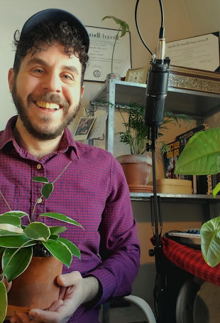 Photo of Zein, smiling and sitting at a desk, with a houseplant in his lap.
