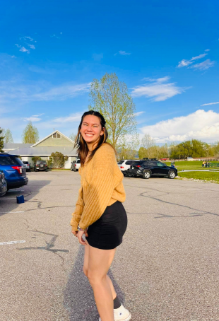 Christi smiling at the camera wearing a yellow sweater and black shorts.
