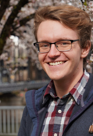 Karl smiling outside, wearing glasses, a plaid button-down shirt, and a blue jacket.