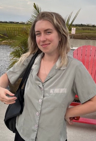 Annie posing outside, wearing a short sleeve gray button-down shirt and holding a black purse.