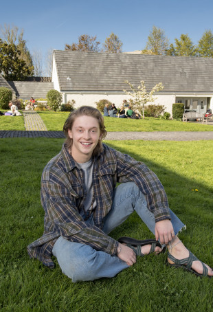 Bode sitting outside Albany Quadrangle. He is wearing a checkered shirt and blue jeans.