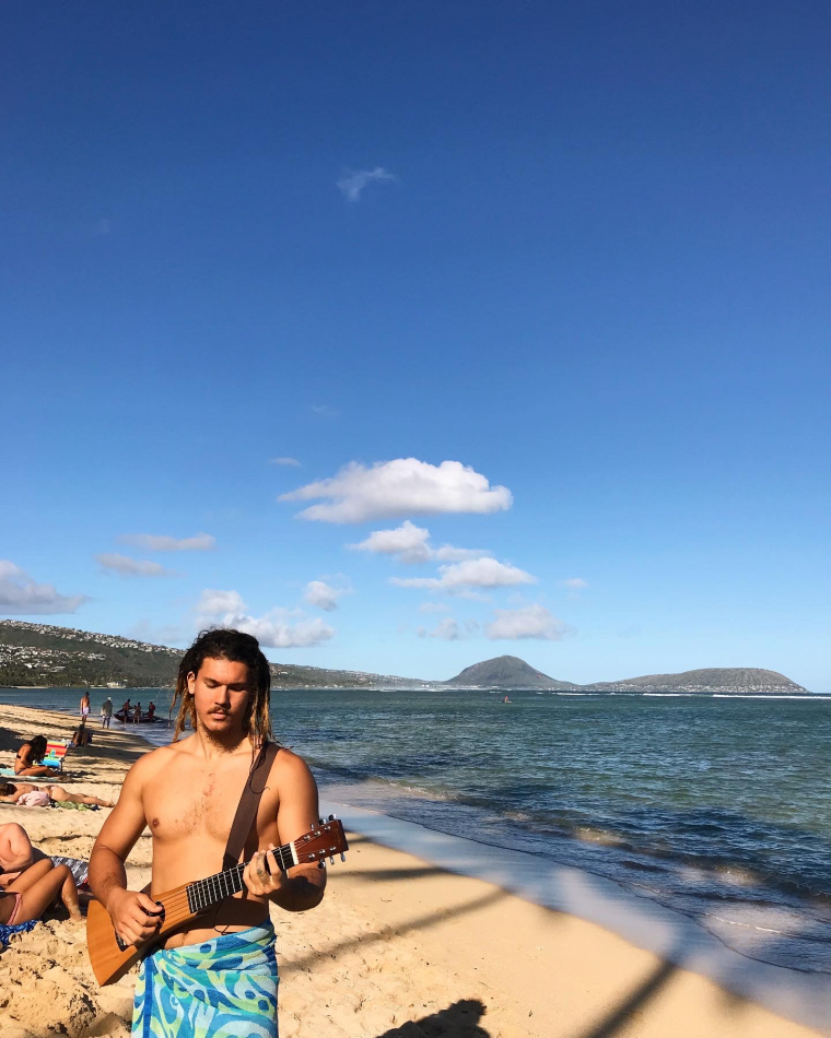 Kepa, standing on a beach, holding a guitar and looking toward the sand. Student-supplied profile...