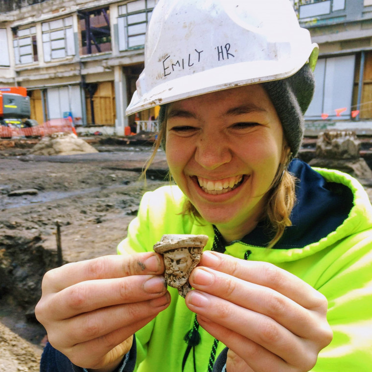 Emily, smiling while wearing construction gear, holding a 19th century pipe head found during an ...