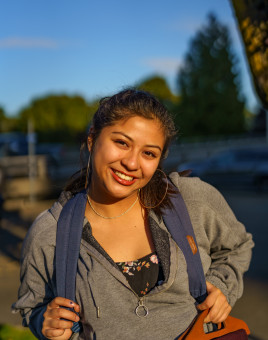 Diana Pacheco smiling, wearing a gray sweater and blue backpack.