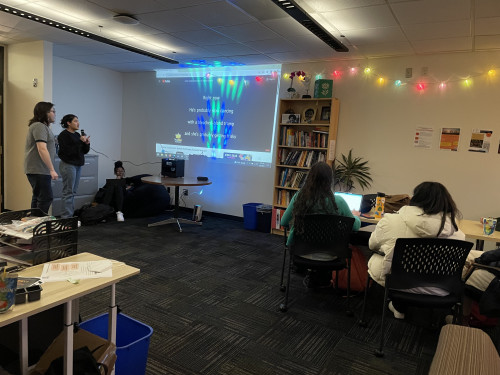 Karaoke Night in the IME Suite. A picture of two students singing in a microphone facing a projector screen with other students observing.