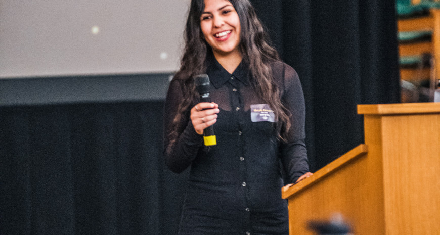 Student keynote speaker Sheyla Dorantes holding microphone behind the podium.