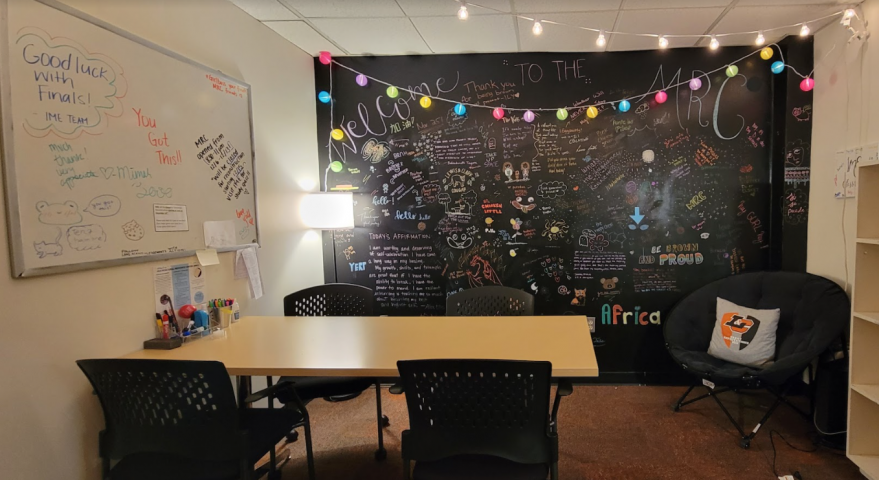 Image: The Multicultural Resource Center (MRC) space with chalk wall, decorative lights, white bo...