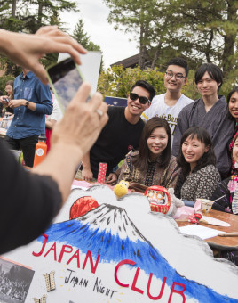 A 2018 photo of the Japan Club smiling and sitting at an outdoor table during Pio Fair.