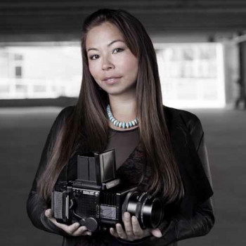 Photo of Matika Wilbur. She is holding a camera in her hands and facing the viewer.