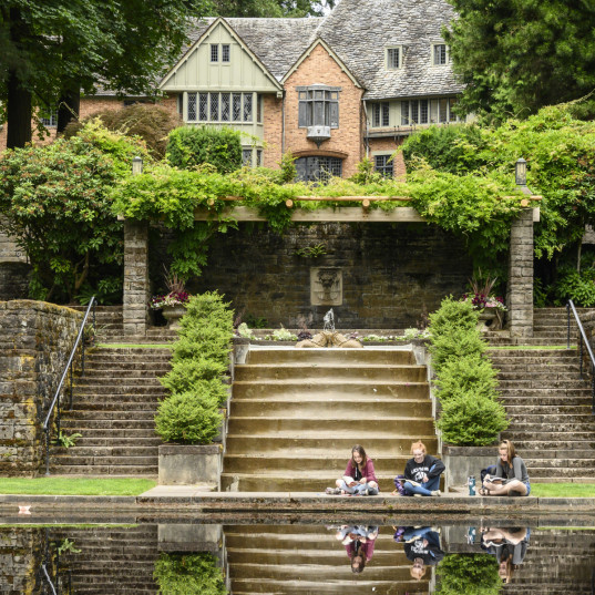 Students sitting by the reflecting pool with the Manor House in the background.