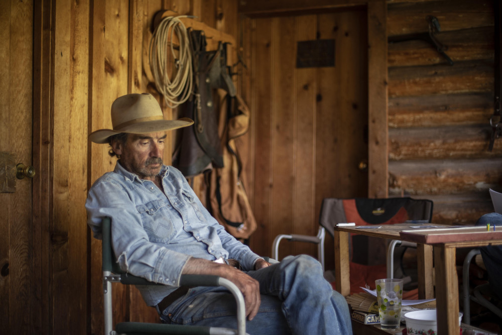 Max sitting on a chair, wearing a cowboy hat, denim button-up shirt, and jeans.