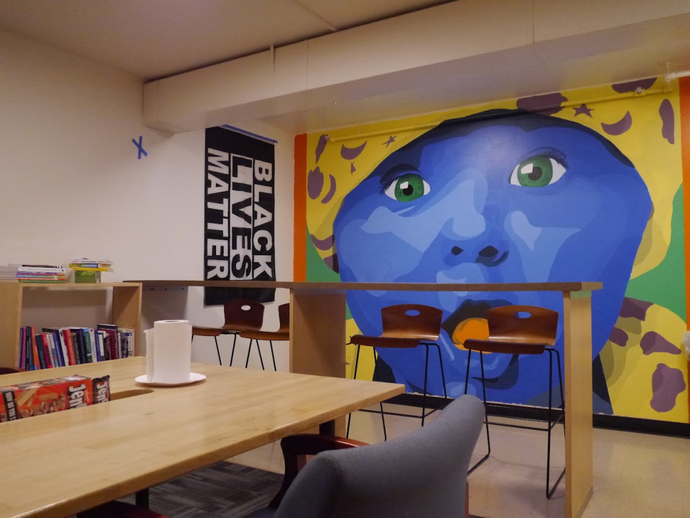 Tables in a room with a large mural of a blue-faced person next to a Black Lives Matter poster hanging on the wall.